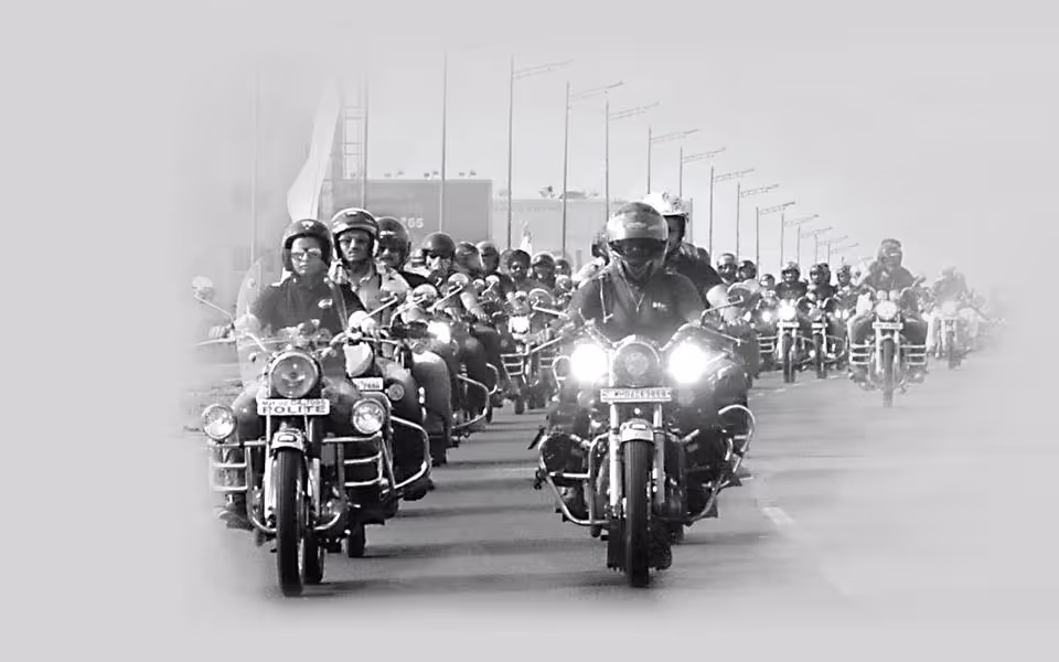 Skupina motorkářů jedoucích v řadě po silnici, všichni v helmách, černobílá fotografie.