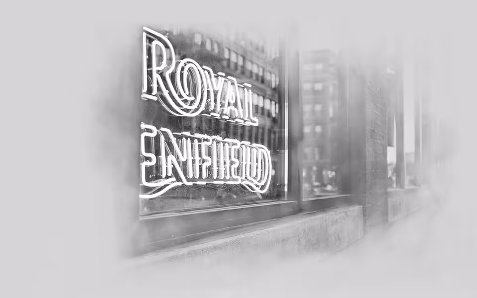 Neonový nápis Royal Enfield na okně budovy v černo-bílé fotografii.