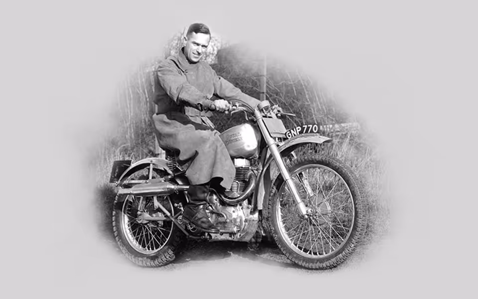 Černobílá fotografie muže v kabátu sedícího na motorce s poznávací značkou GNP 770.
