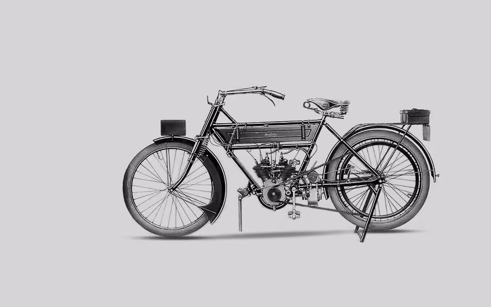 Historický černobílý obrázek starého motocyklu s viditelným detailem motoru a tenkými pneumatikami.