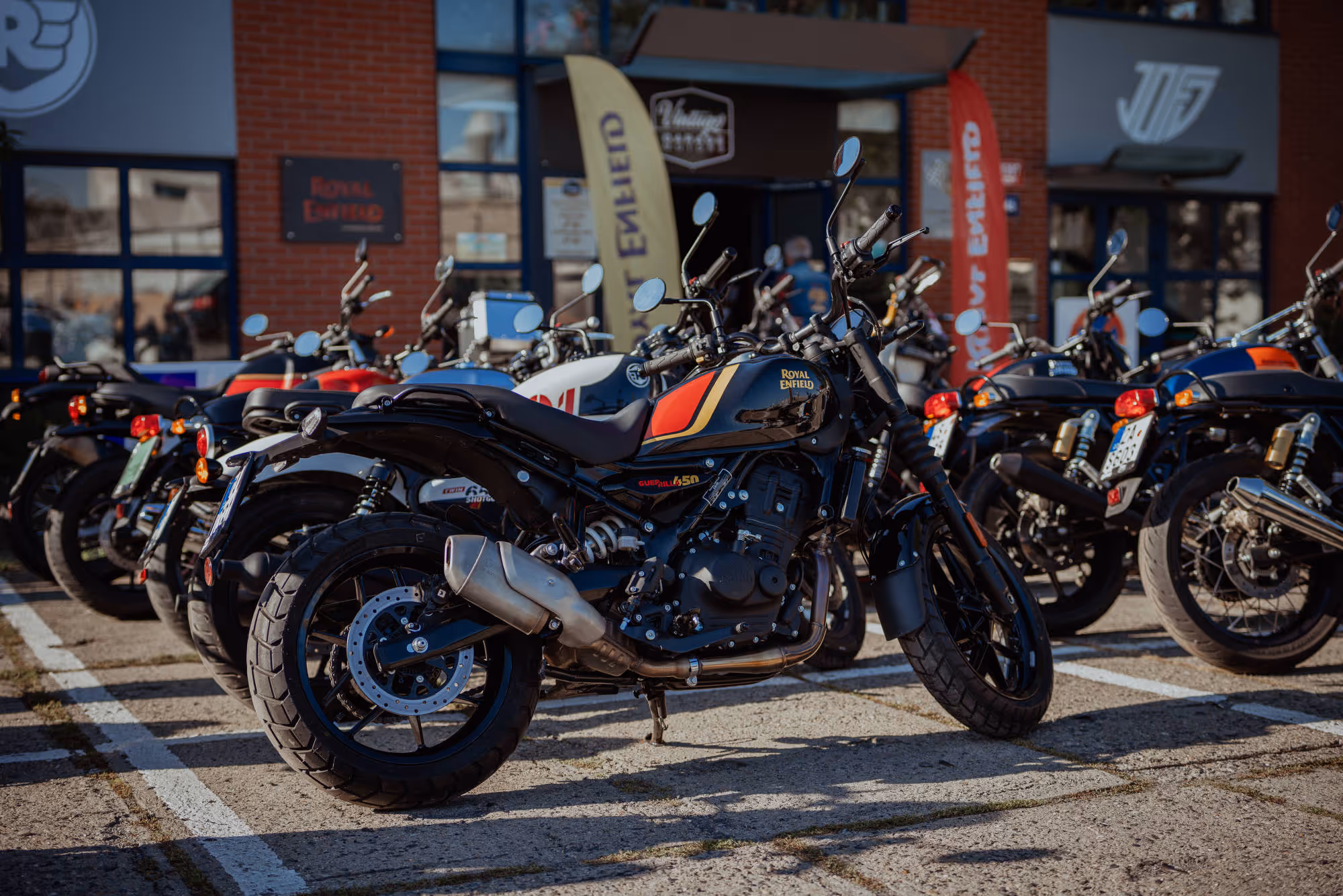 Černá a červená motorka Royal Enfield zaparkovaná vedle dalších motorek před budovou s nápisem Royal Enfield.