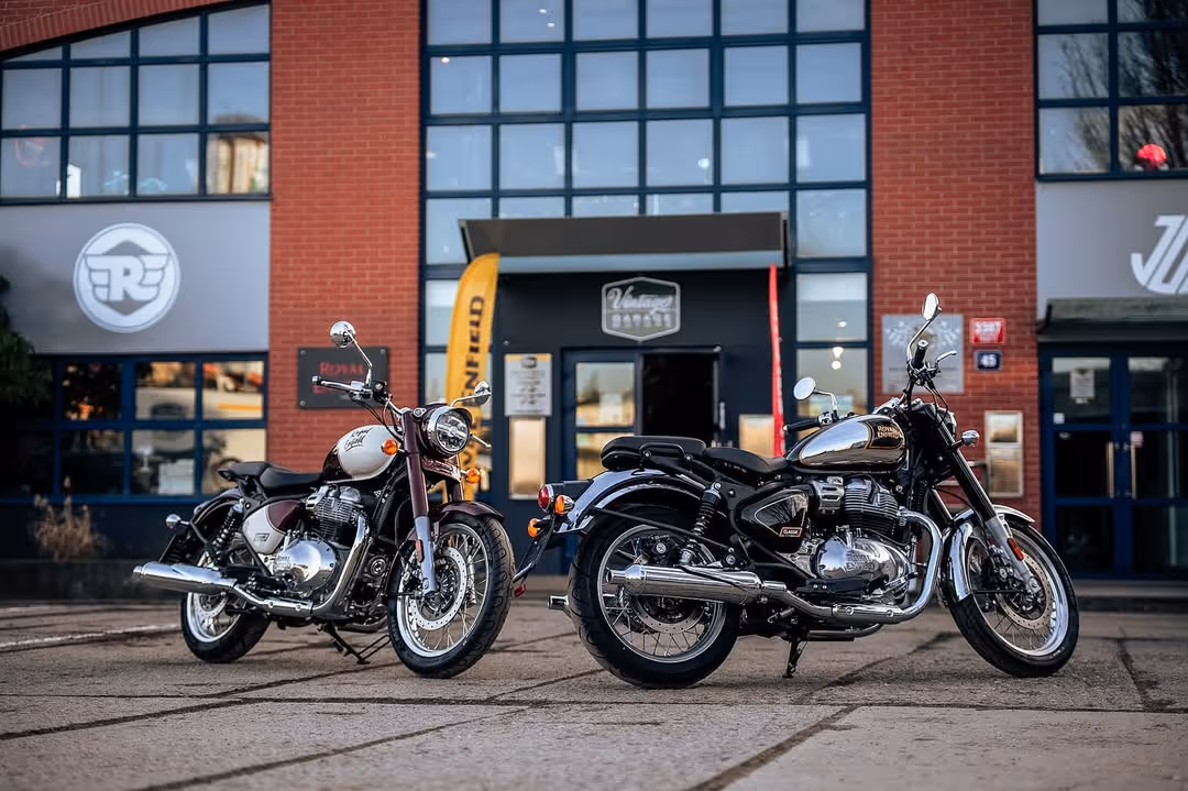 Dvě černobílé a chromované retro motocykly zaparkované před moderní budovou s velkými okny.