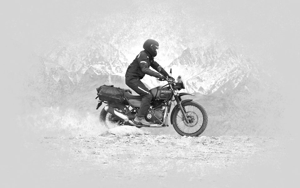 Jezdec na motocyklu Royal Enfield Himalayan na prašné cestě pod zasněženými horami