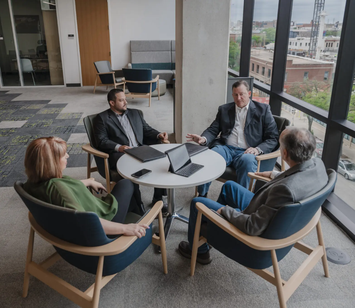 CNF team in casual meeting around white table with laptops in modern office with city views