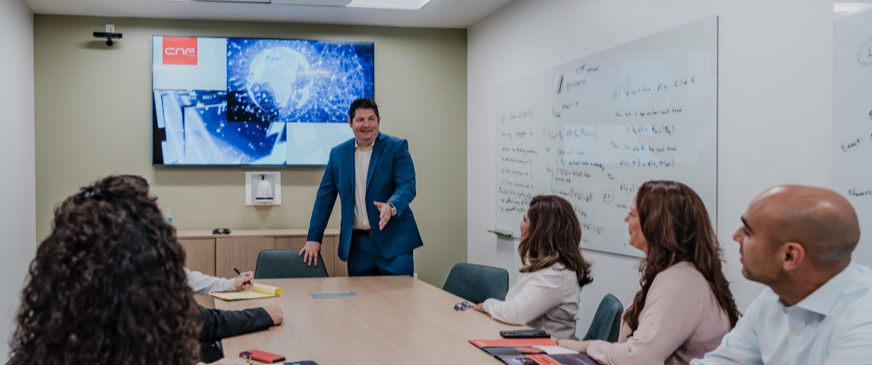 Jason G. presenting to the CNF team in conference room with digital display and whiteboard.