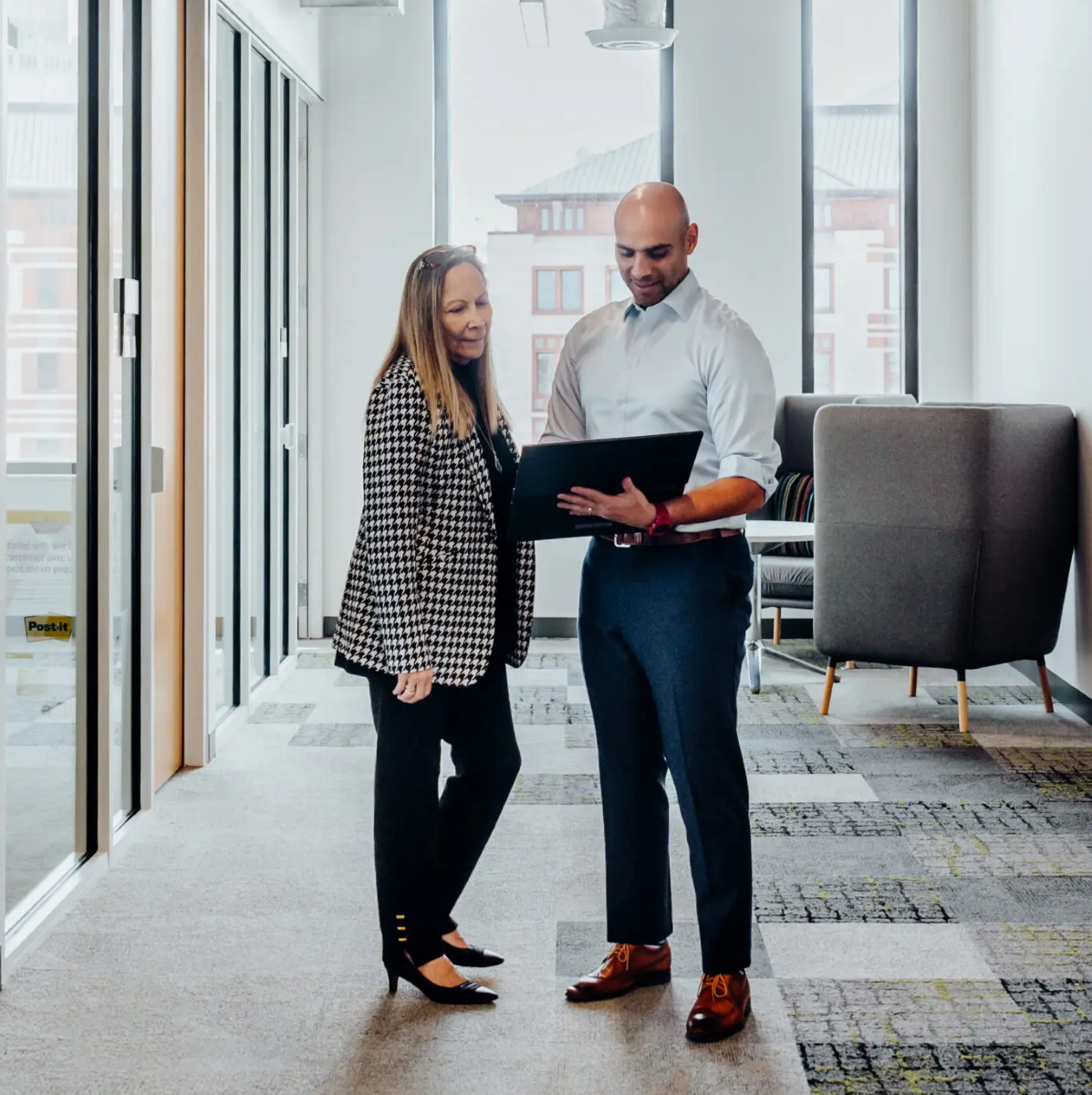 Roxanne and Freddy reviewing a tablet together in a modern office hallway.