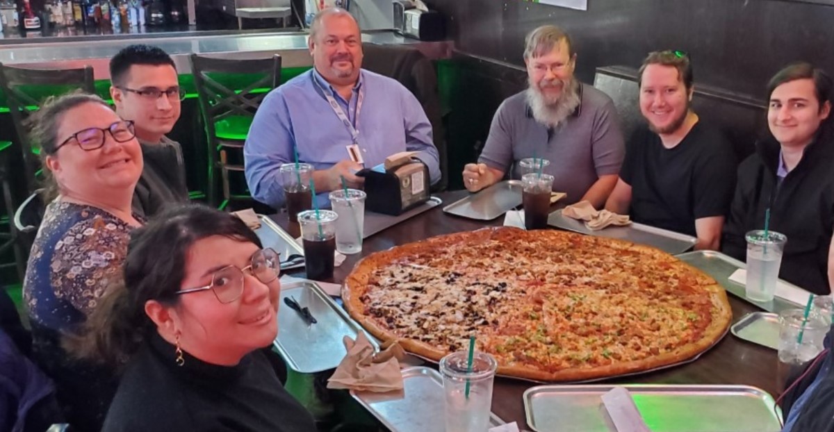 CNF team celebration dinner with large pizza and smiling group members