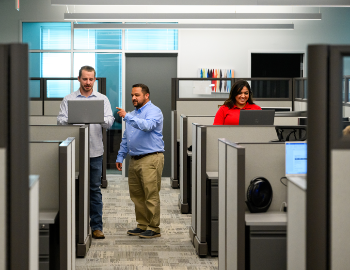 CNF Employees in modern office cubicles, one holding laptop, collaborating in workspace.