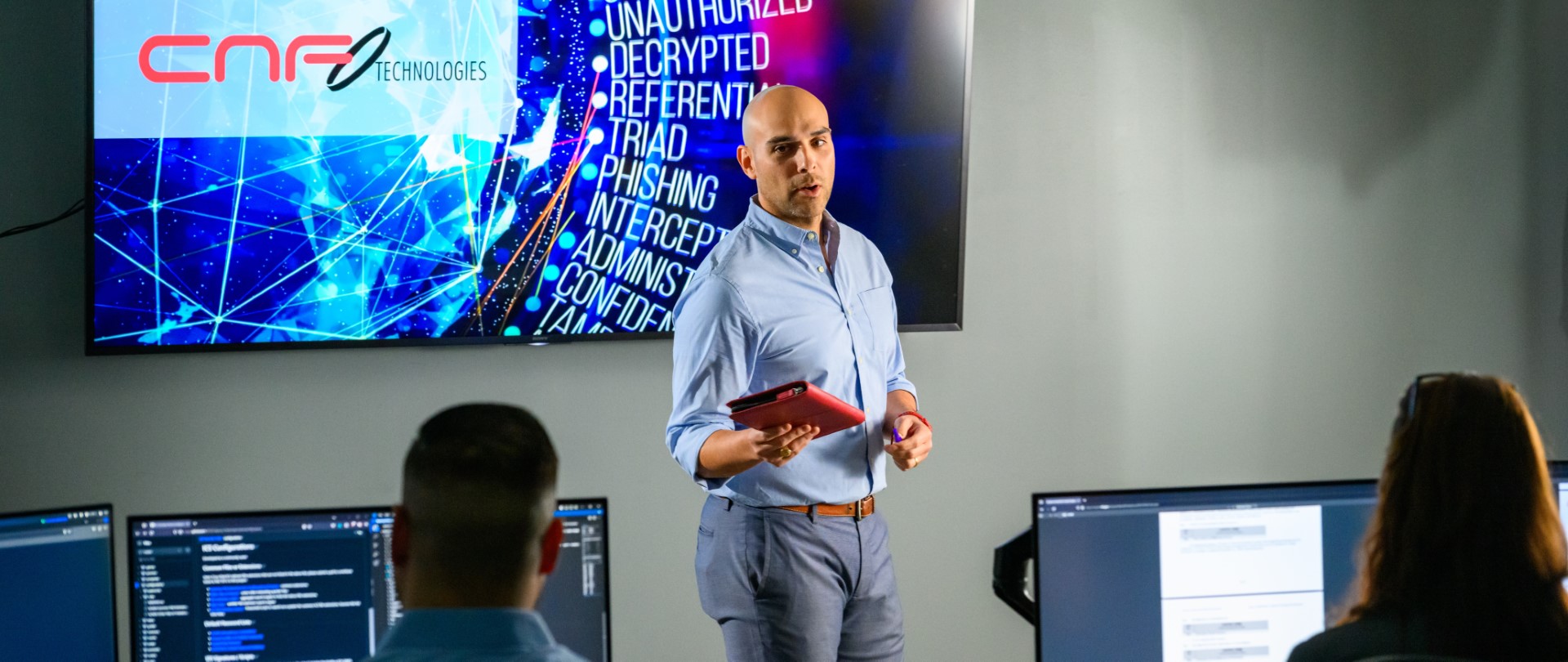 Freddy Ramirez presenting with a red tablet in front of a screen showing CNF Technologies logo and security terms.