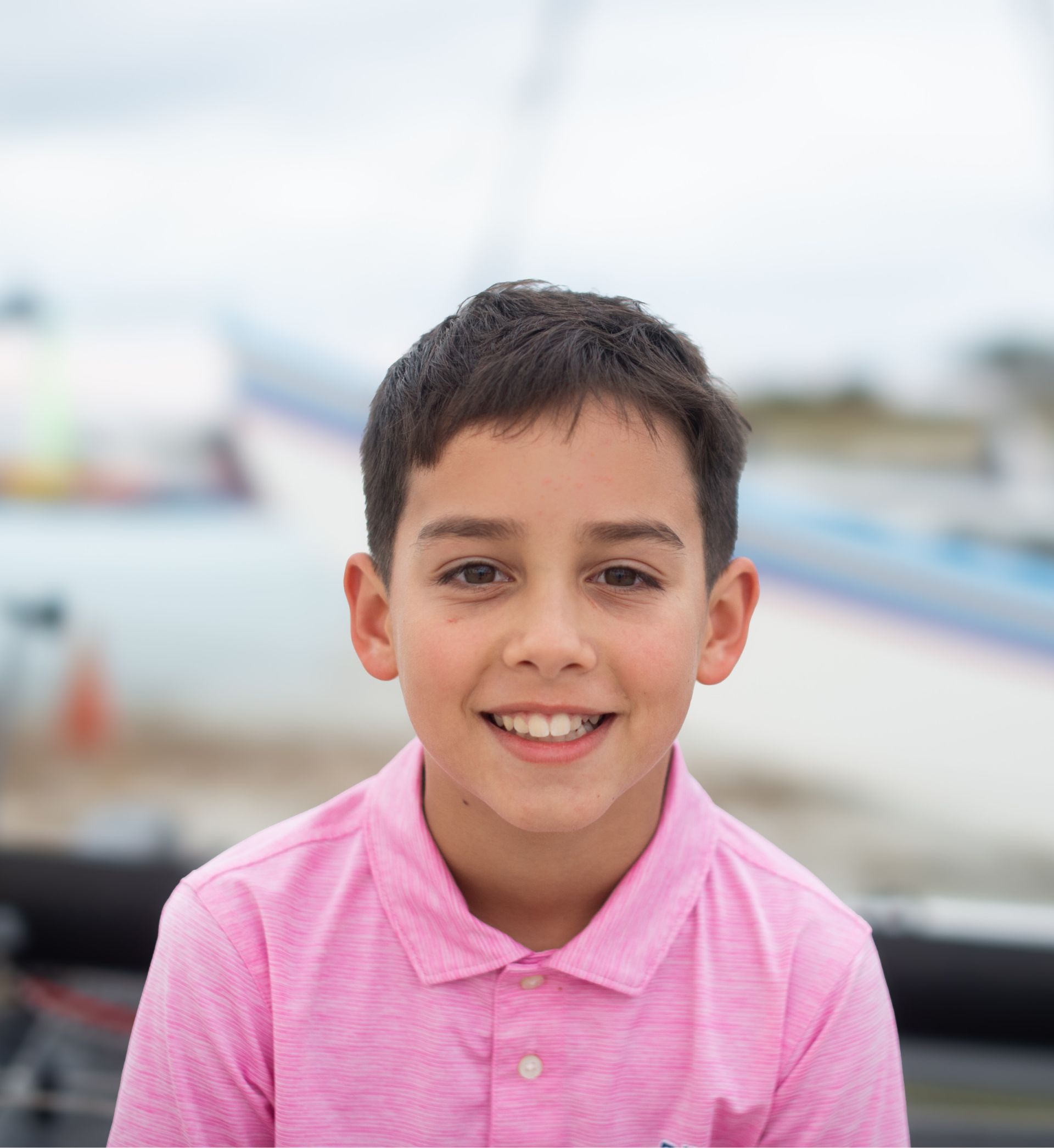 Smiling young boy with short dark hair wearing a pink polo shirt outdoors.
