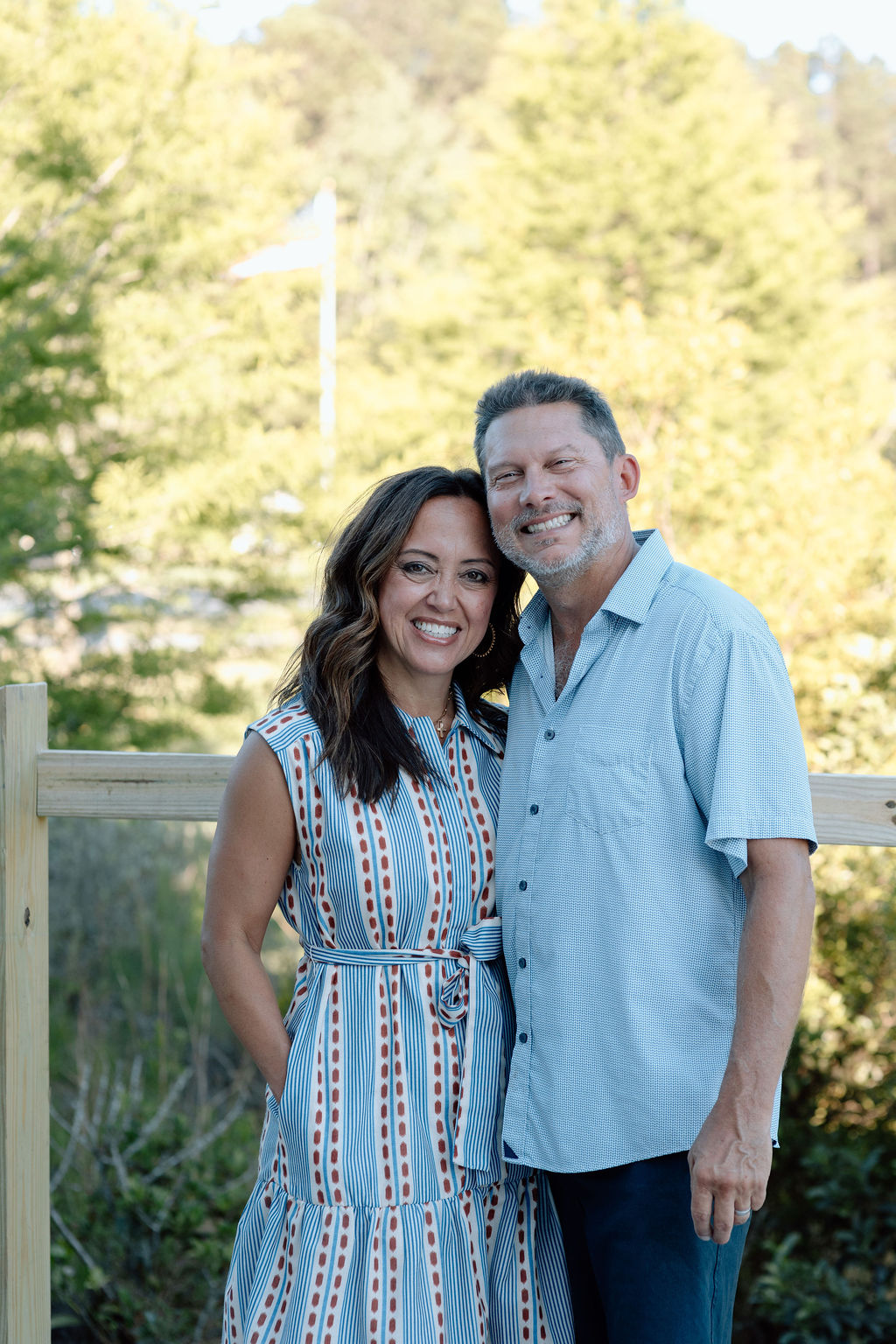Smiling couple embracing outdoors with blurred green trees in the background.