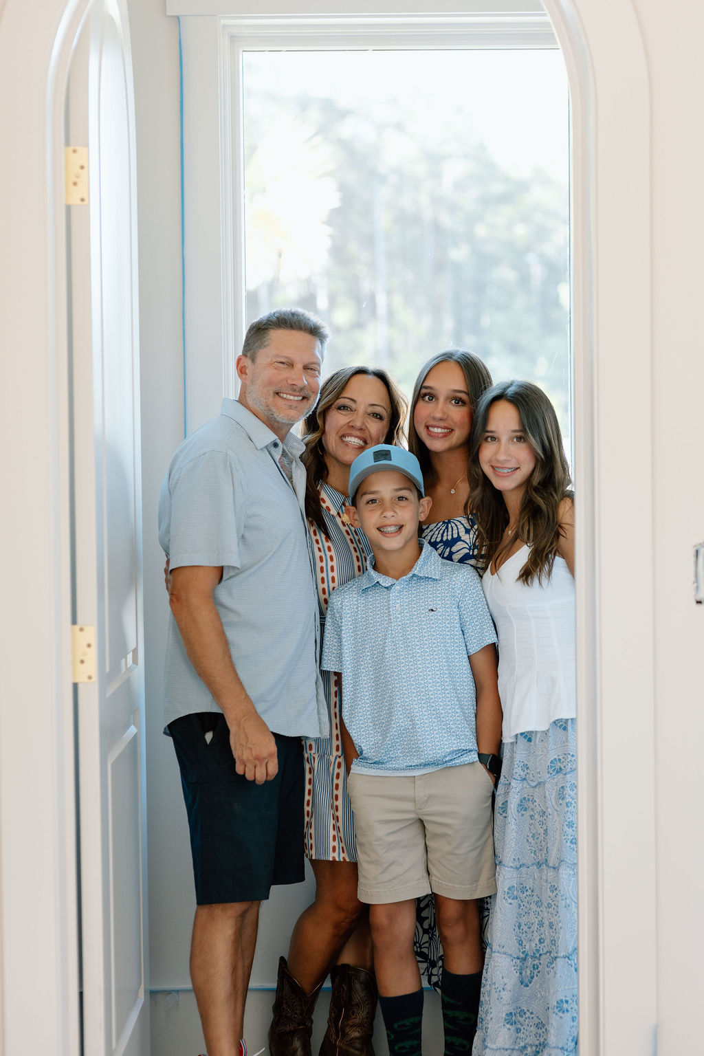 Smiling family of five posing together by a window in a bright room.
