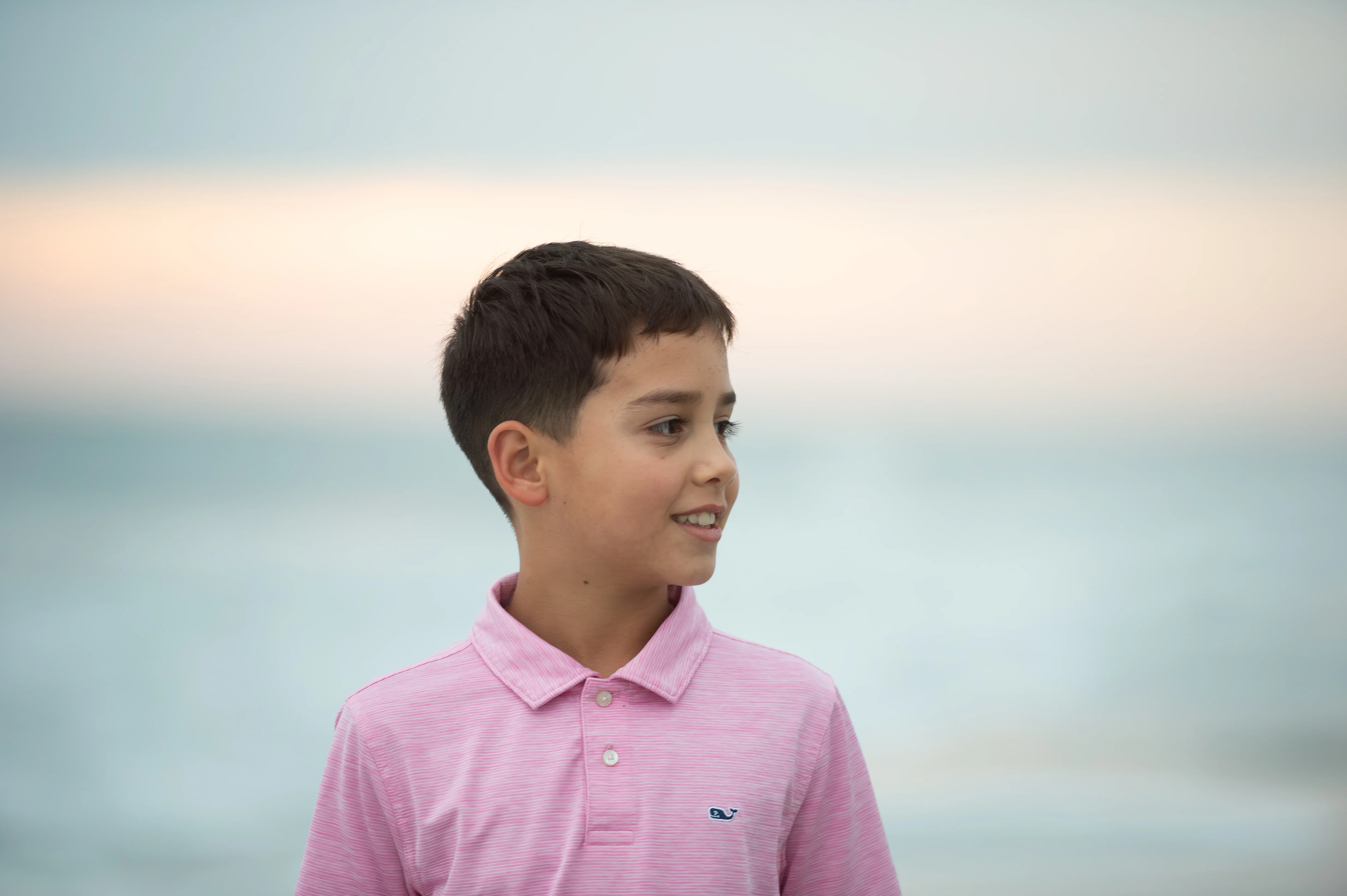 Young boy in a pink polo shirt looking off to the side near the beach
