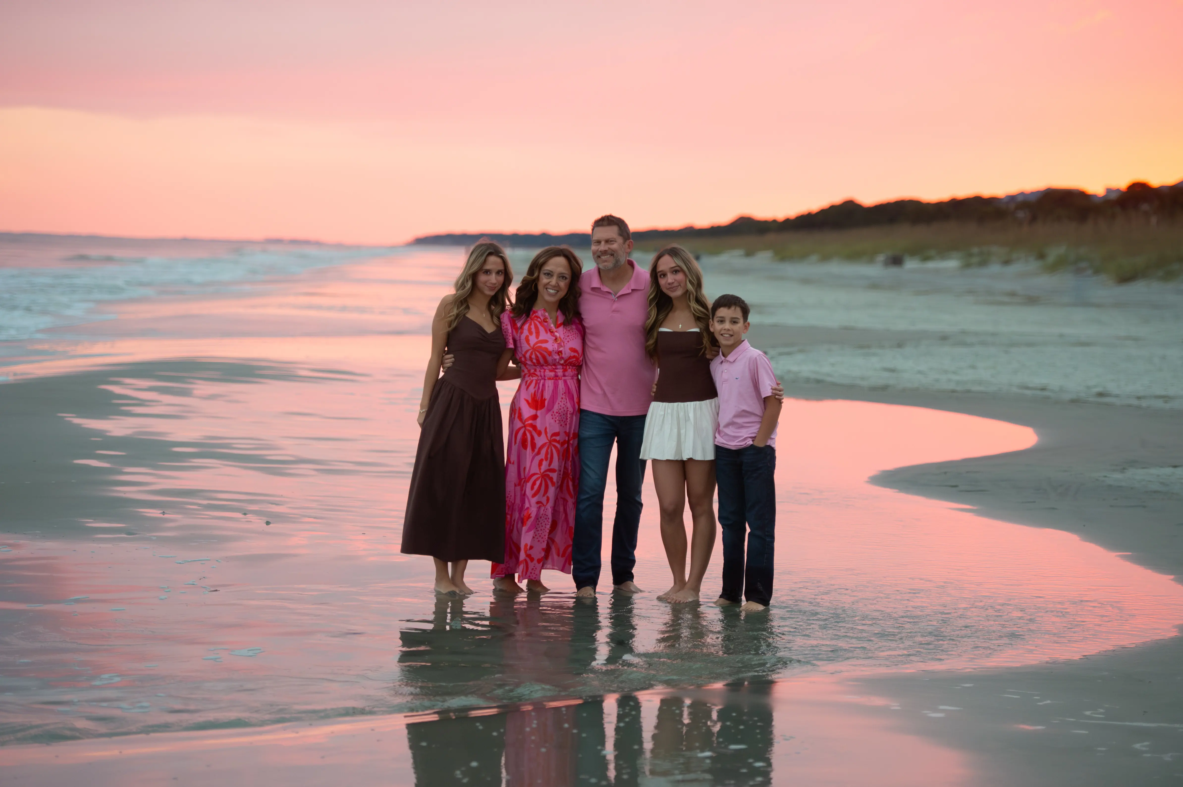 Family of five posing together on the beach at sunset under a pink sky