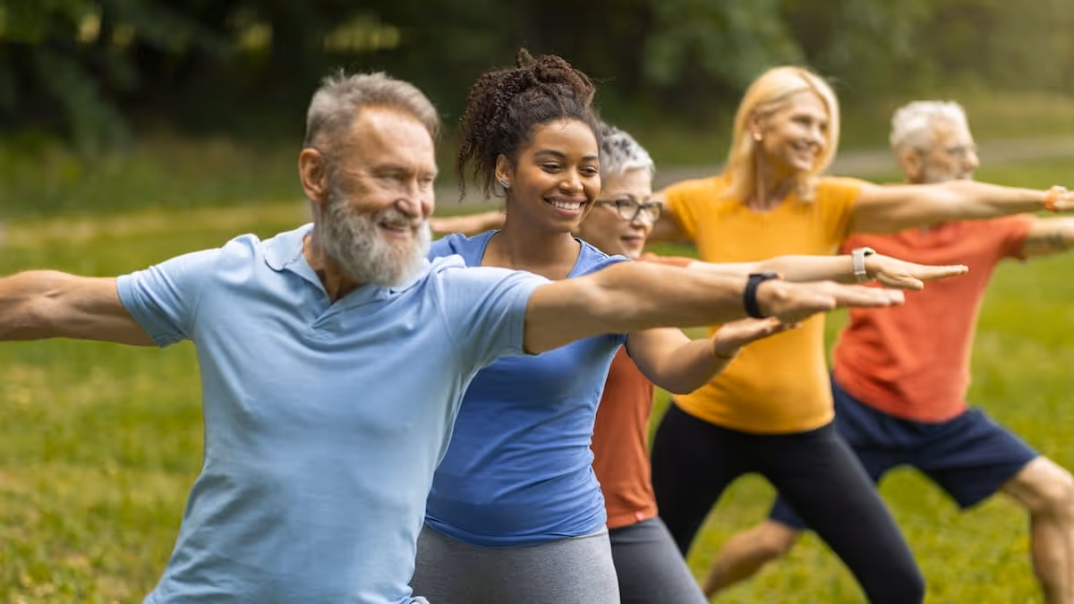 Group of diverse adults practicing yoga in a park, standing in Warrior II pose with arms extended.