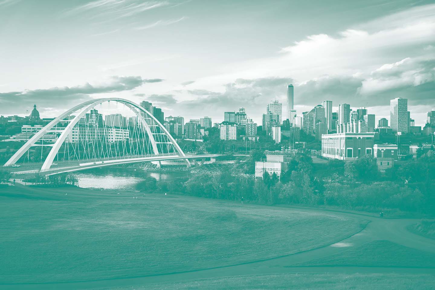 City skyline with a modern white arch bridge over a river and green parkland in the foreground.