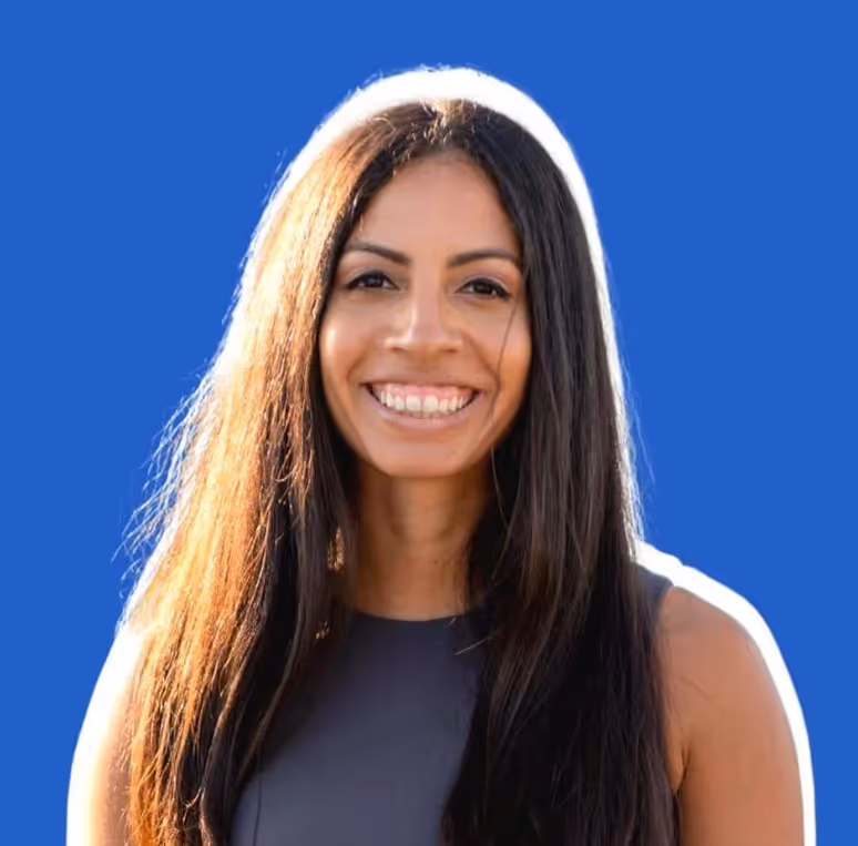 Smiling woman with long dark hair wearing a sleeveless dark top against a blue background.