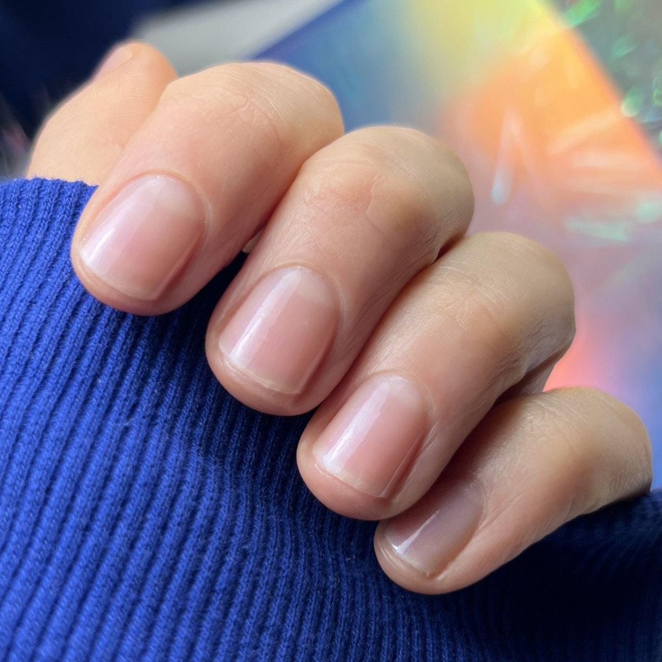 Close-up of a hand with clean, natural nails resting on a blue knitted fabric.