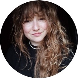 Smiling woman with long curly light brown hair wearing a black top and a pearl necklace.