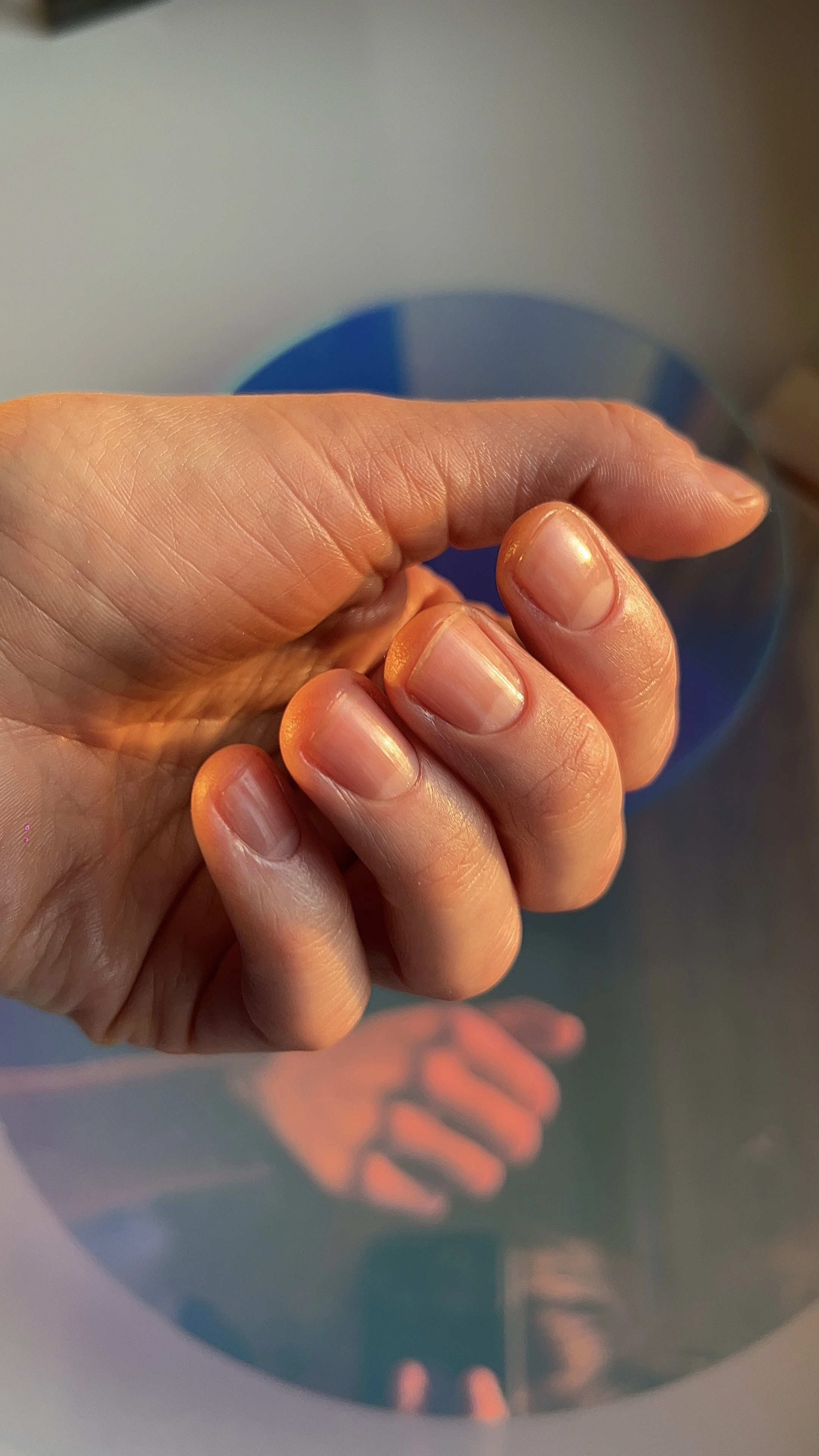 Hand with neatly trimmed nails reflected in a round mirror, illuminated by warm light.