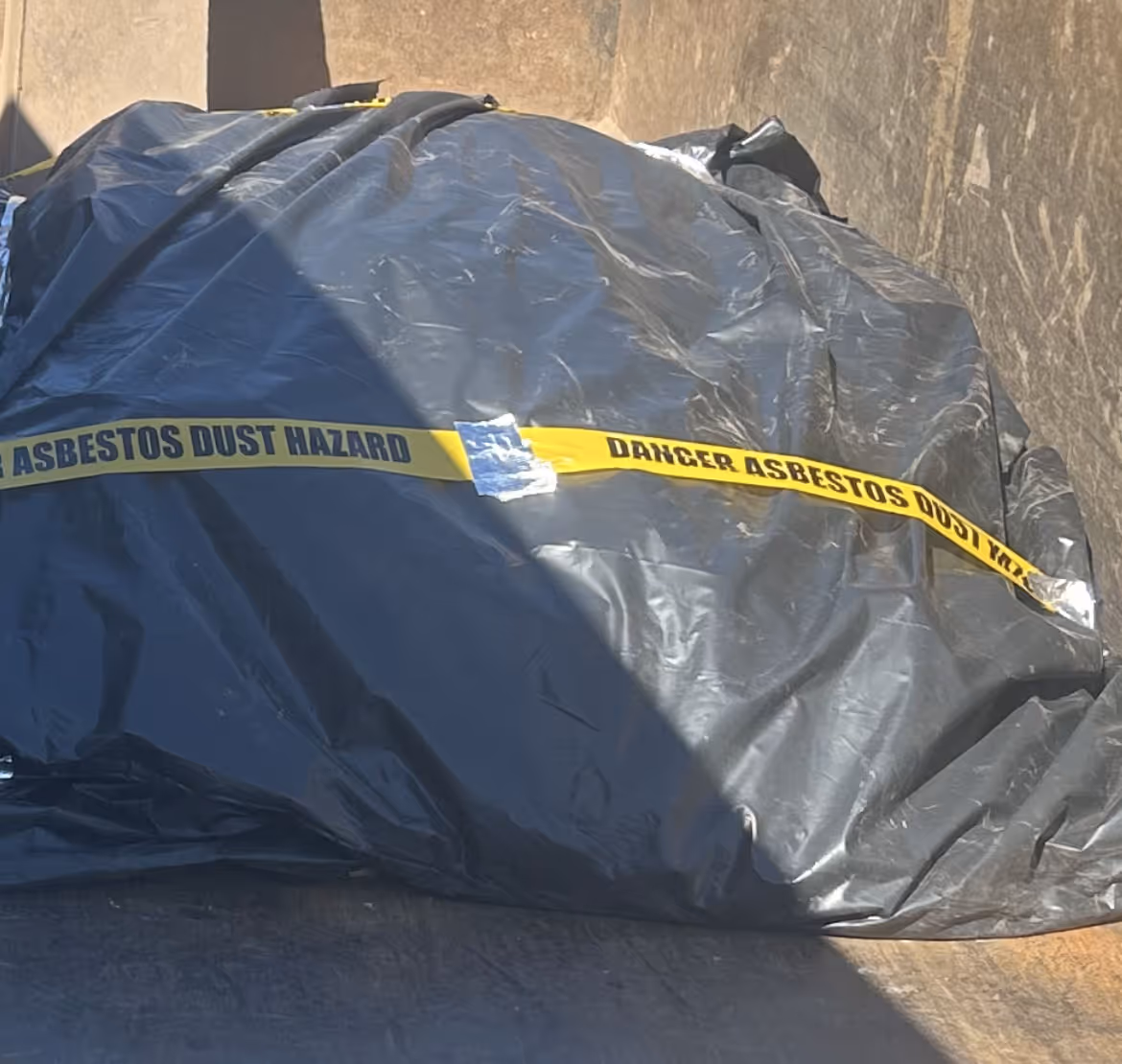 Black plastic-wrapped bundle with yellow tape labeled Danger Asbestos Dust Hazard.