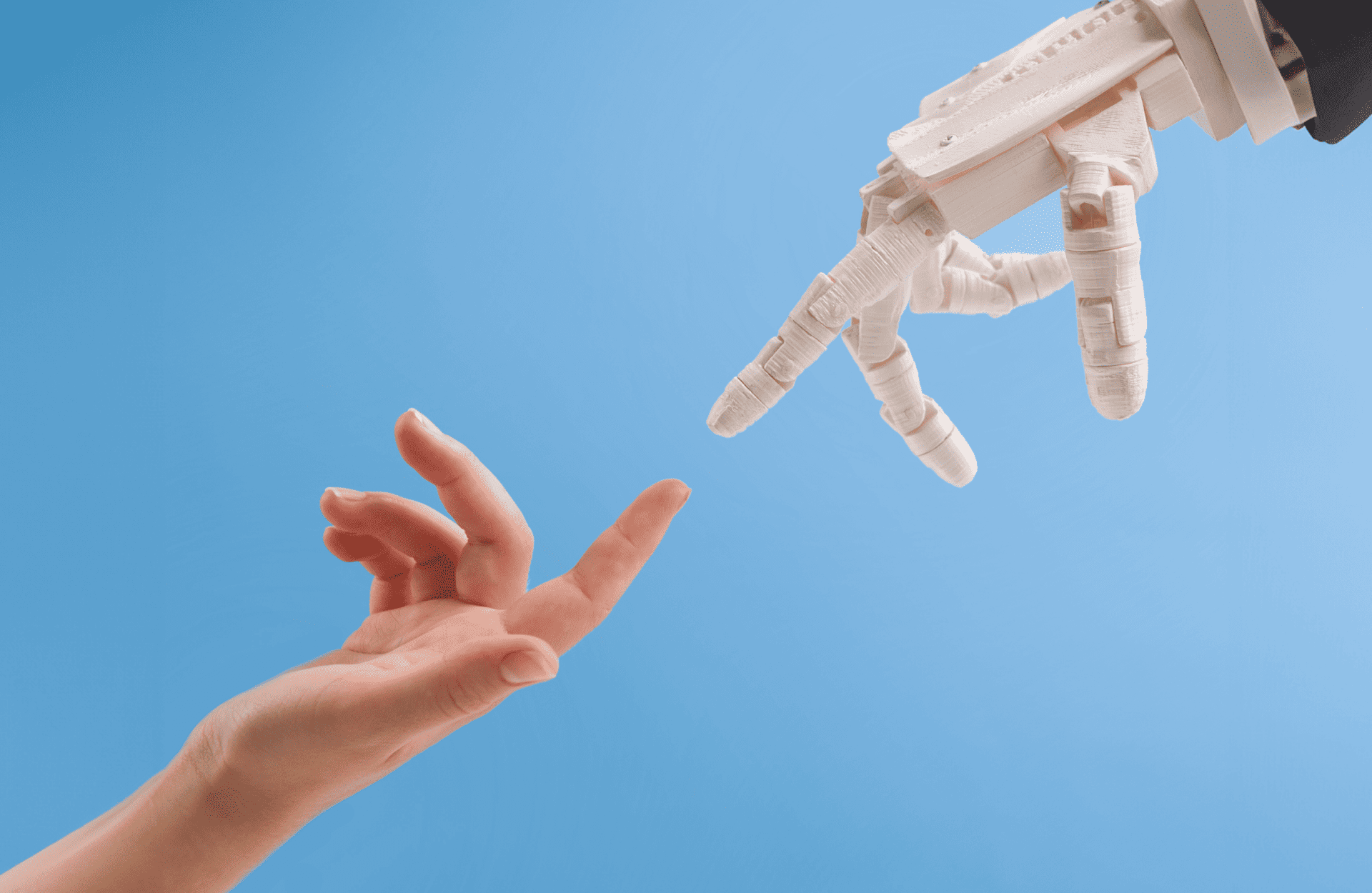 A human hand and a robotic hand reach towards each other against a clear blue background, conveying a sense of connection between technology and humanity.