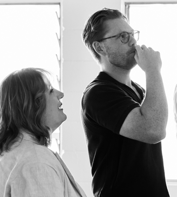 Black and white photo of woman smiling and man with glasses thinking with hand near mouth.