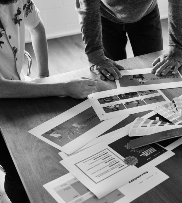 Two people review printed photos, layouts, and color swatches on a wooden table.
