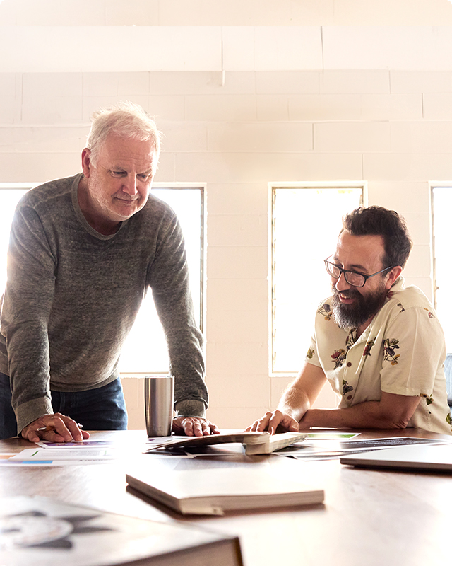 Two men reviewing documents together at a bright, modern workspace with notebooks and a laptop nearby.