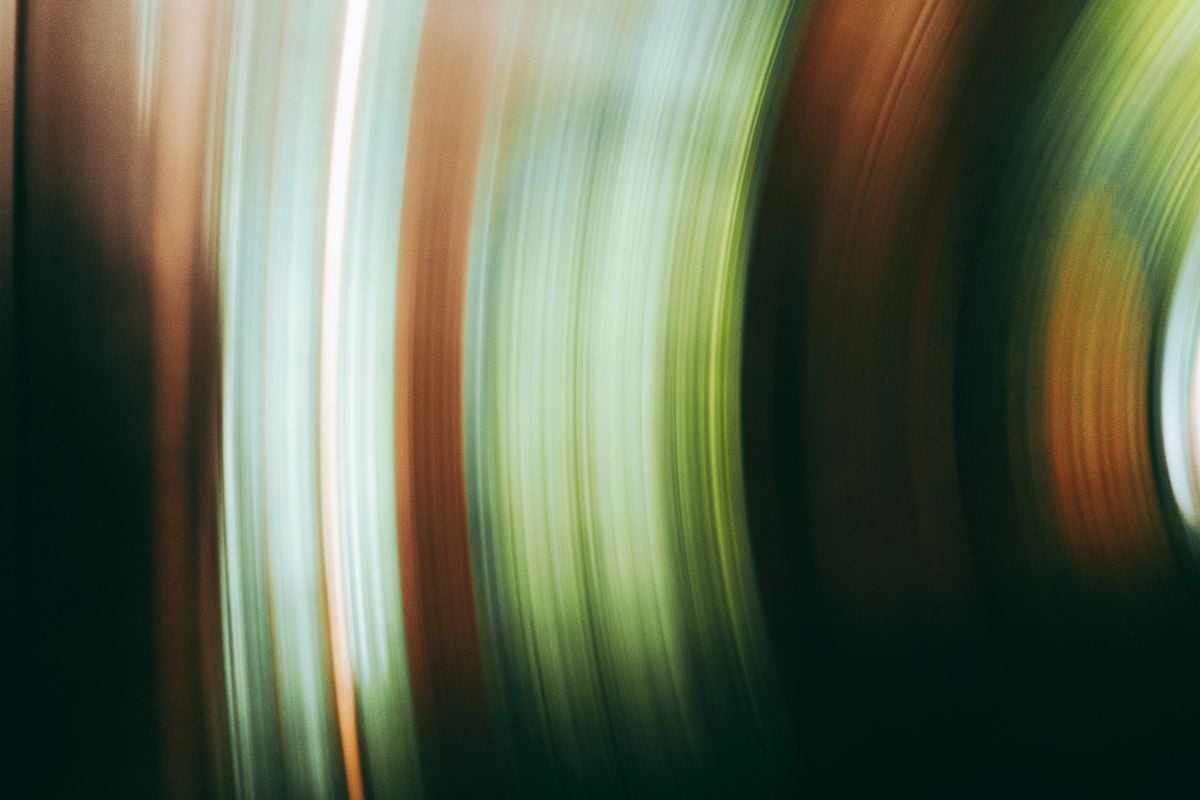Abstract image with curved vertical streaks of green, brown, and light blue colors against a dark background.