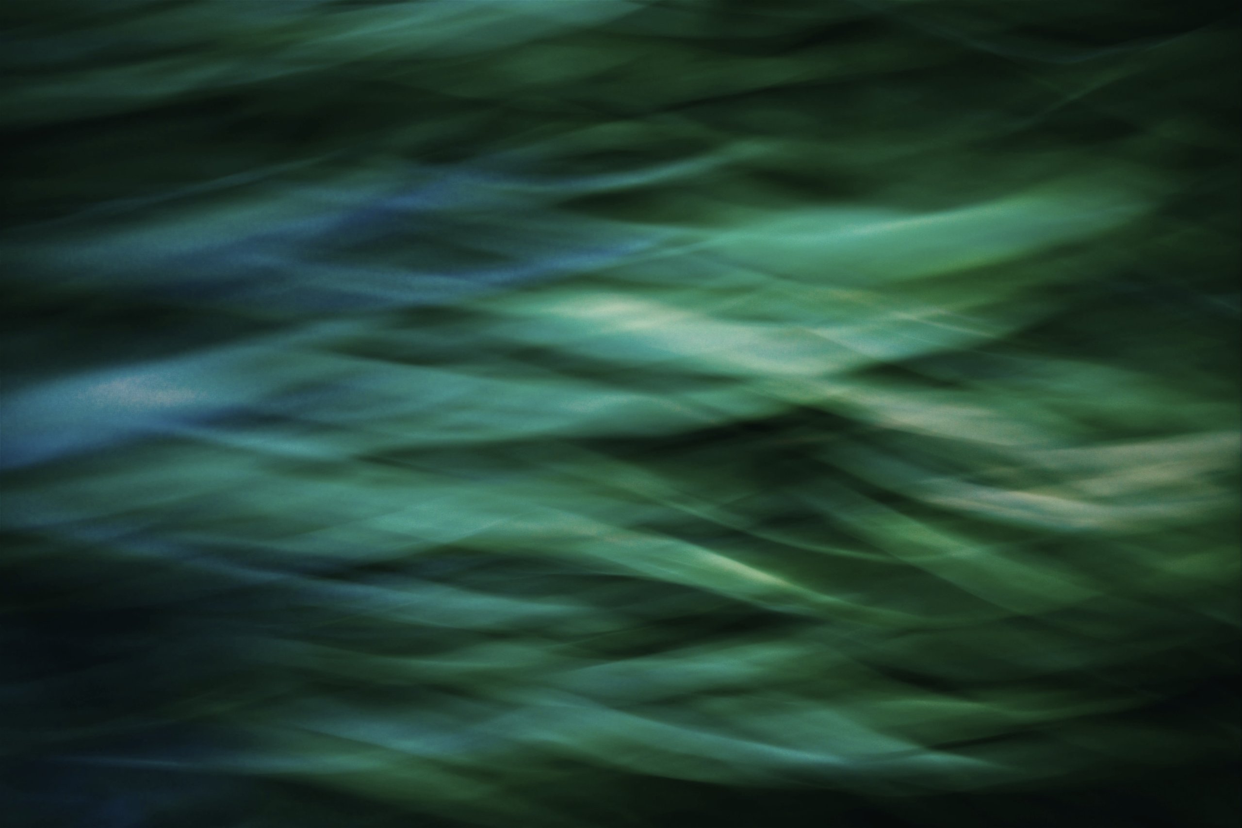 Abstract blurred green and blue light patterns creating a flowing, wave-like effect.