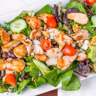 Grilled chicken salad with mixed greens, cherry tomatoes, cucumber slices, walnuts, and feta cheese.