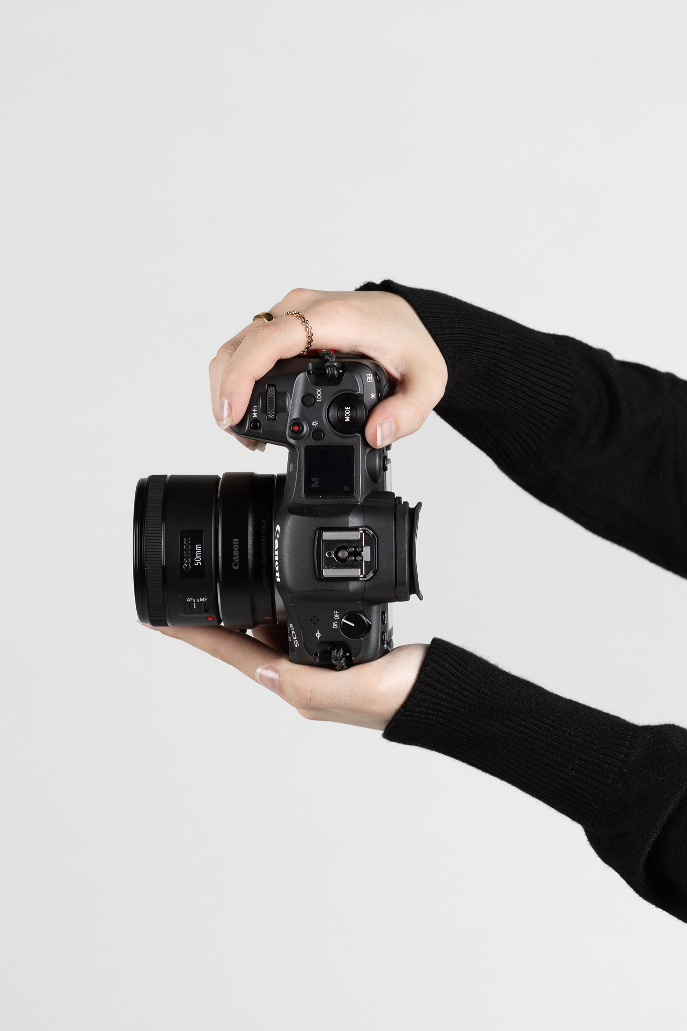 Hands holding a Canon EOS camera with a 50mm lens against a plain white background.