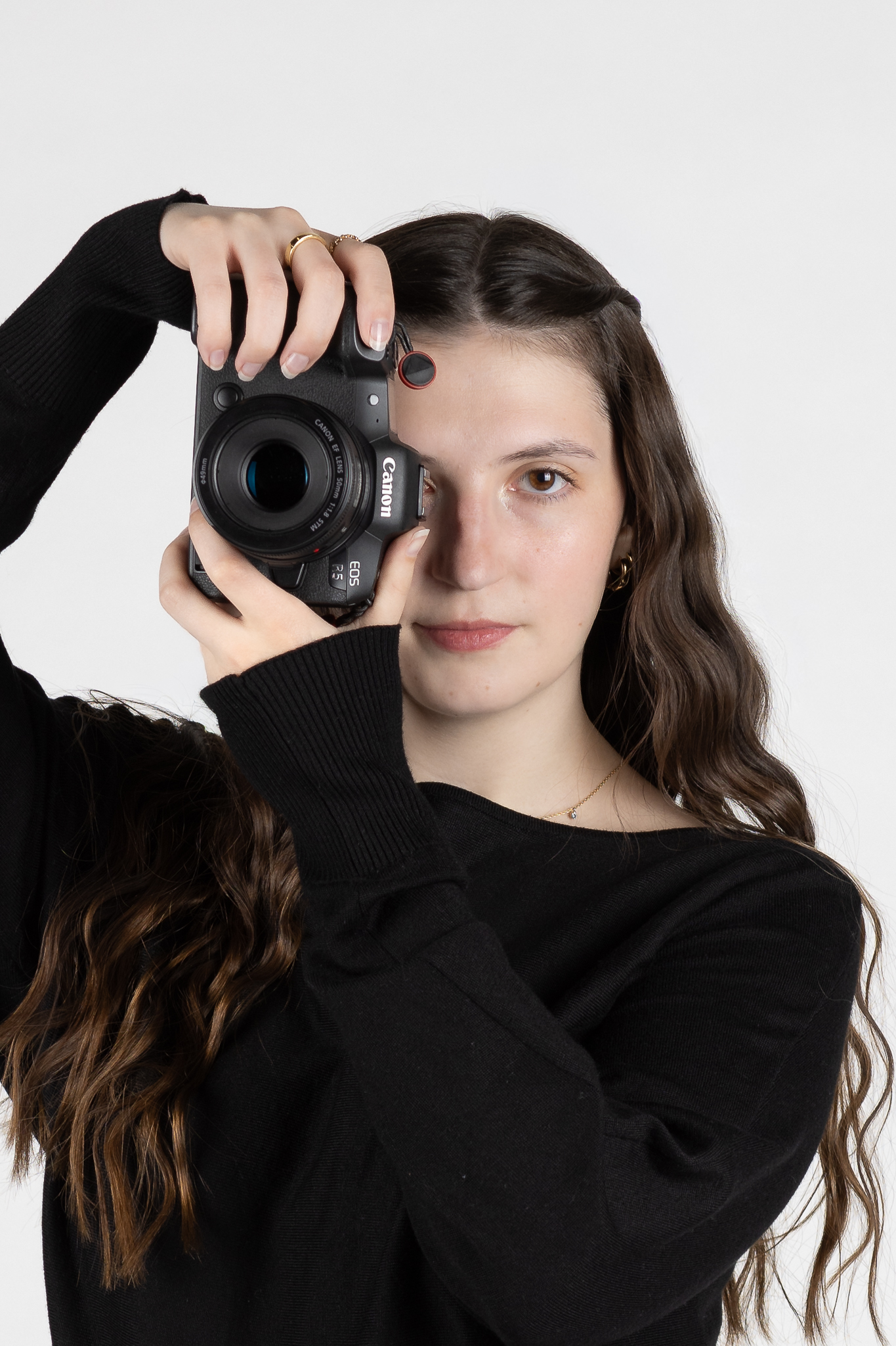 Woman with long wavy hair holding a Canon EOS R5 camera in front of her face.