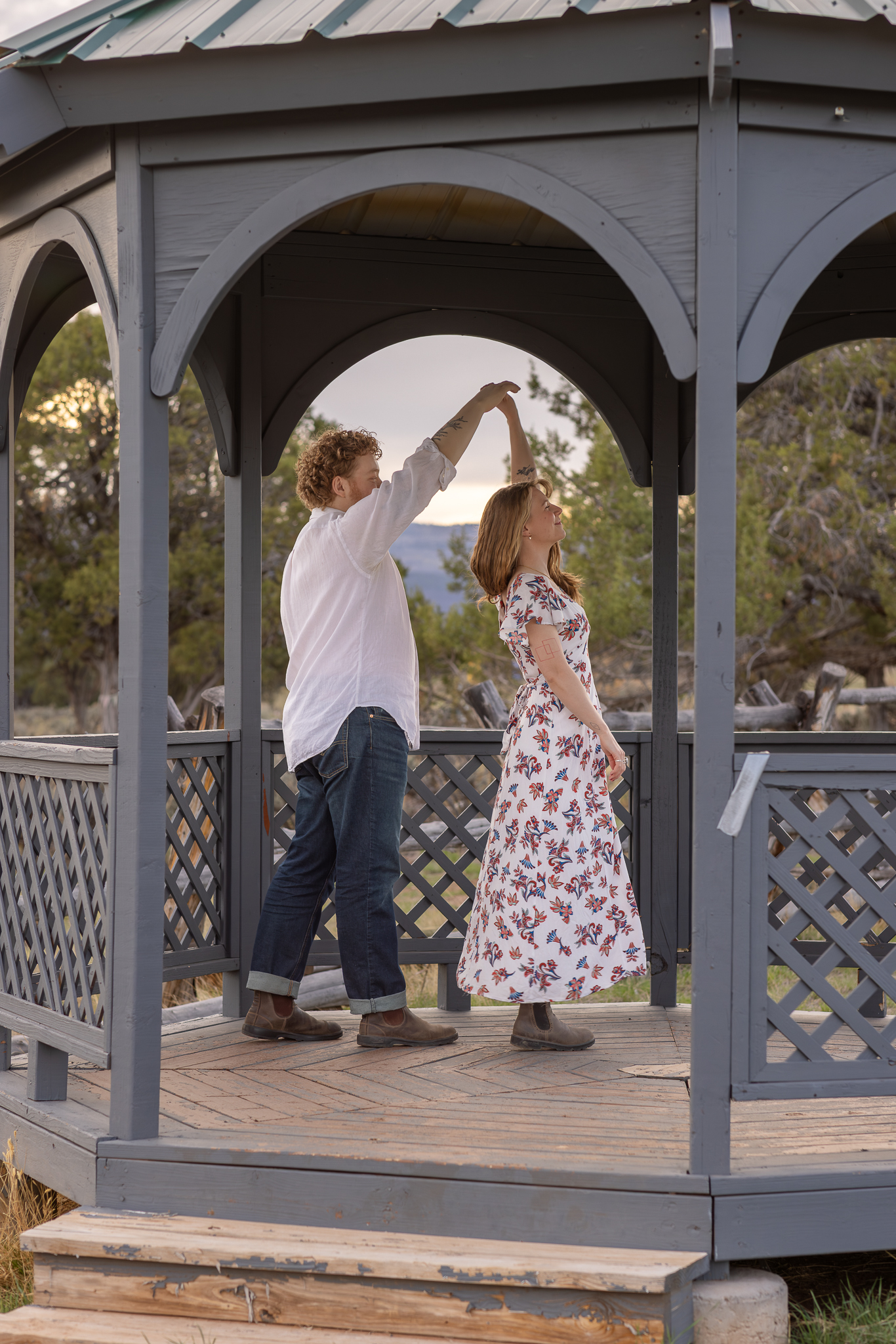 Couple dancing inside a gray wooden gazebo in an outdoor setting during sunset.