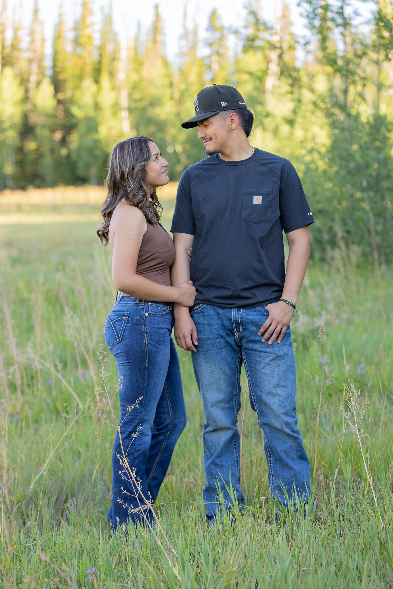 Young couple standing in a grassy field looking at each other affectionately.