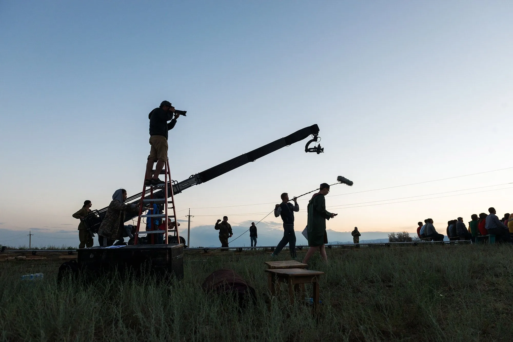 Silhouetted film crew operating a camera crane on location at dusk