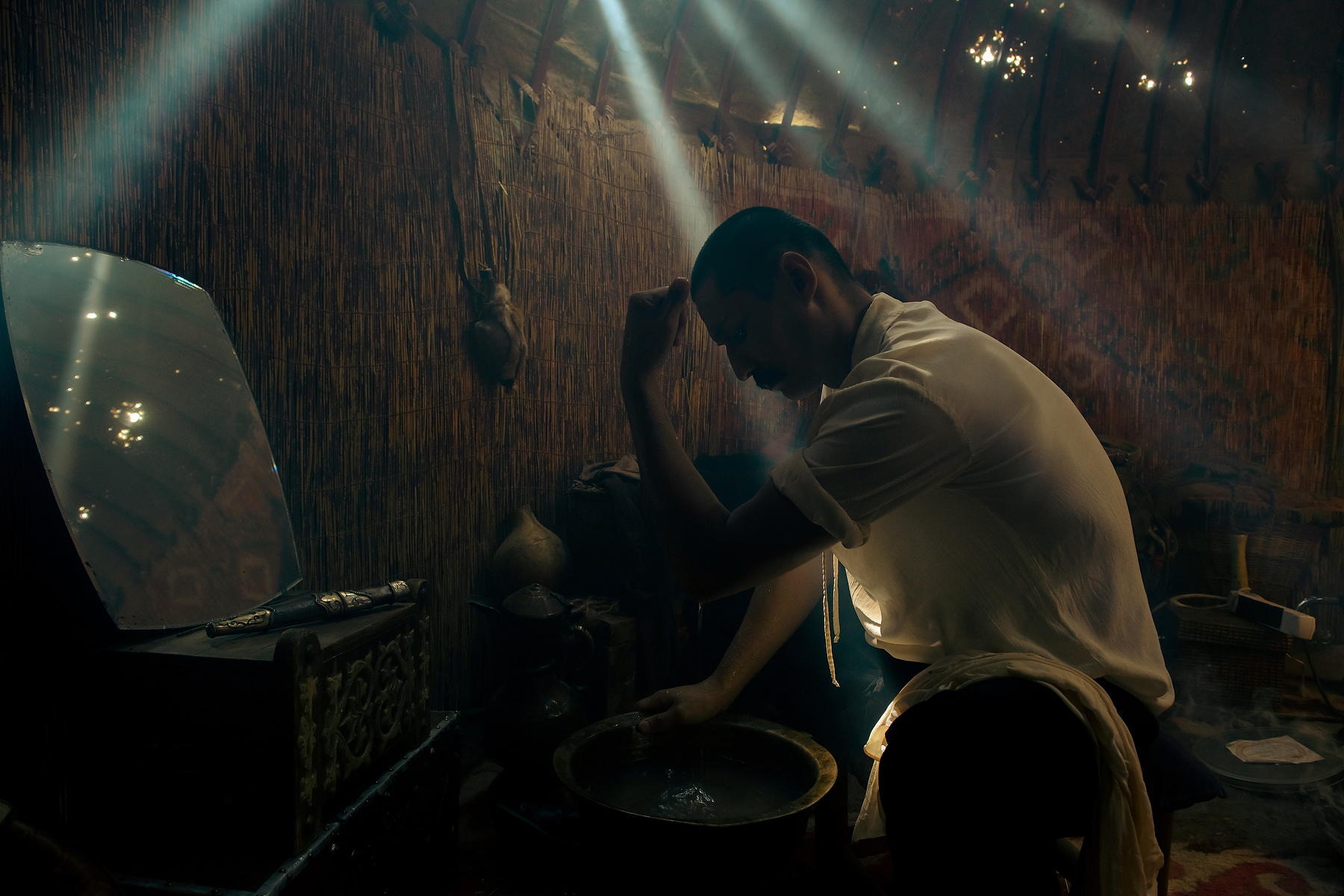 Cinematic unit still of an actor seated inside a dimly lit practical set