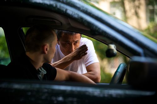 Director giving notes to a performer beside a car during production