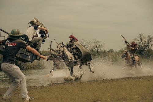 Behind-the-scenes view of a camera crew filming horse riders crossing water