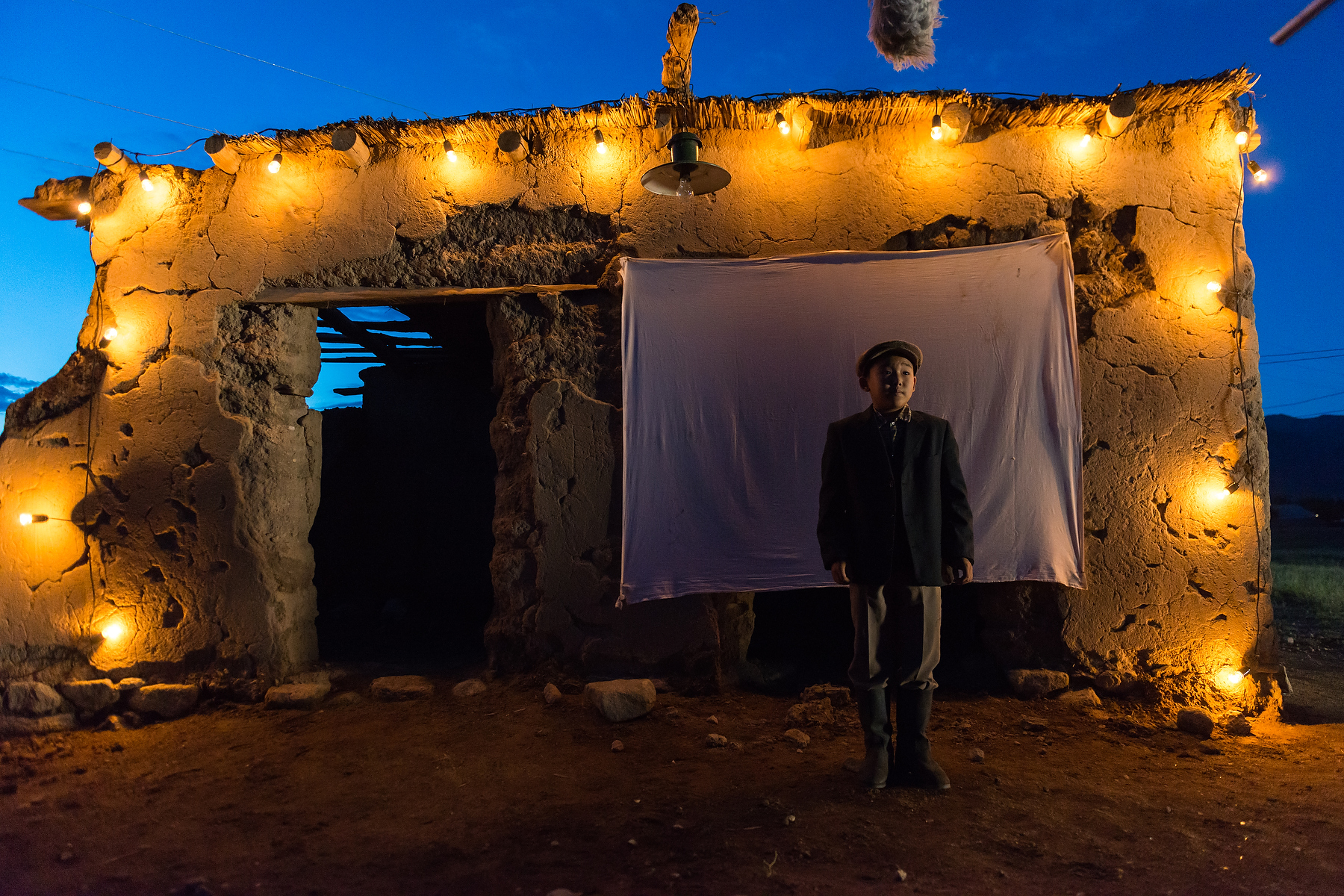 Actor standing on a night exterior film set lit by practical bulbs