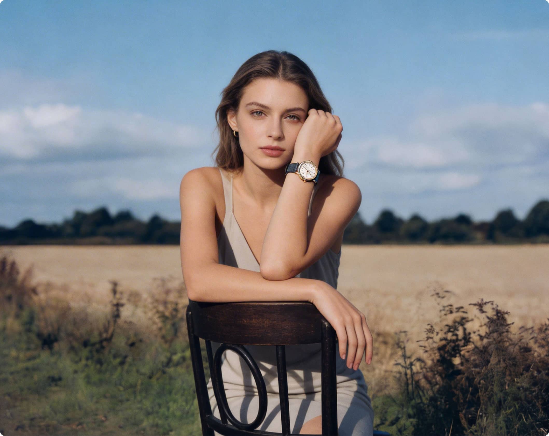 Young man with tousled hair wearing a blue sweater with the word 'GARM' and striped pants, standing outdoors in a field under a blue sky.