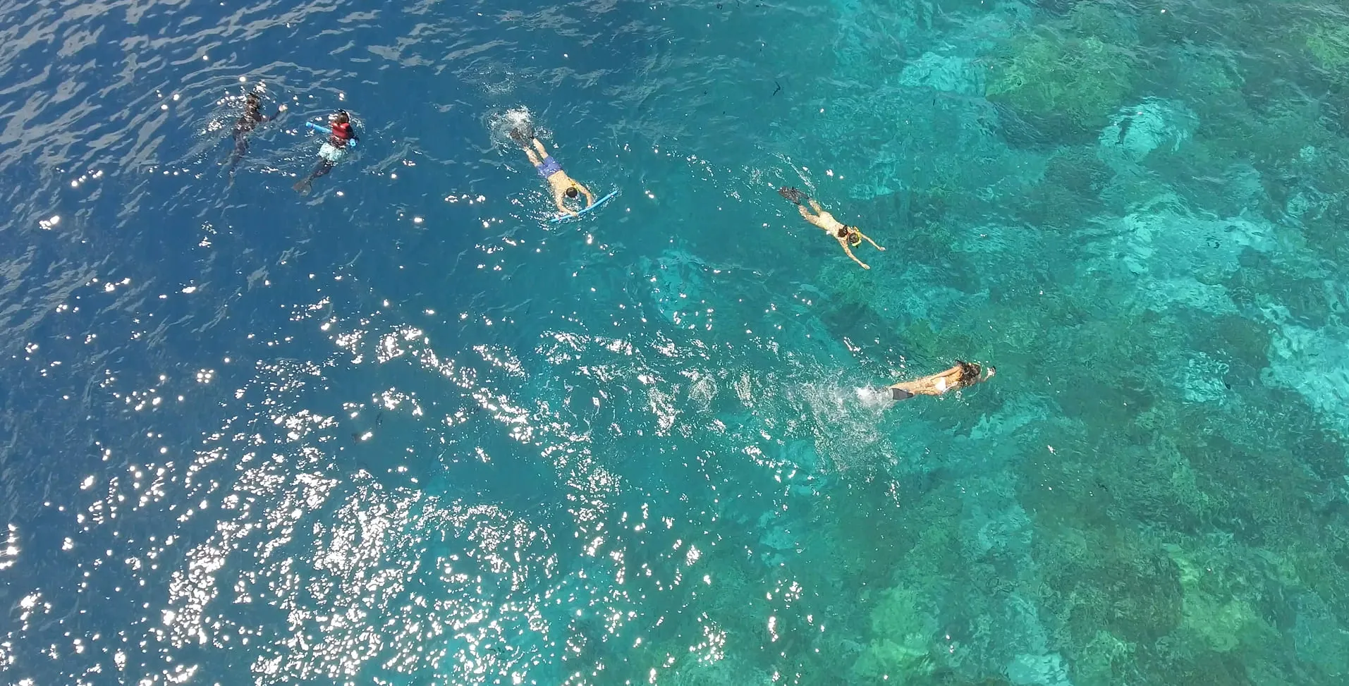 Aerial view of five snorkelers swimming over clear turquoise water with coral reefs visible below.