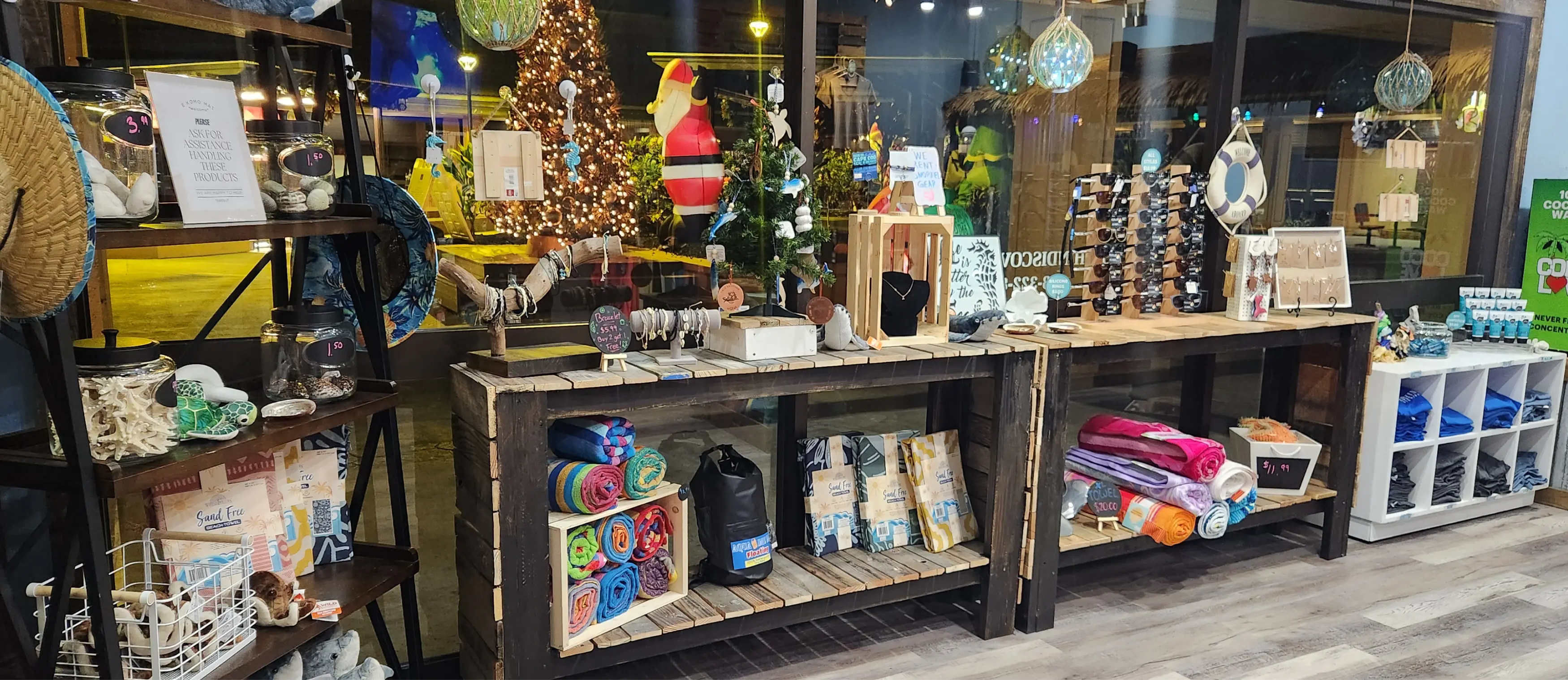 Shop display with beach towels, bracelets, sunglasses, jewelry, and assorted souvenirs on wooden shelves.