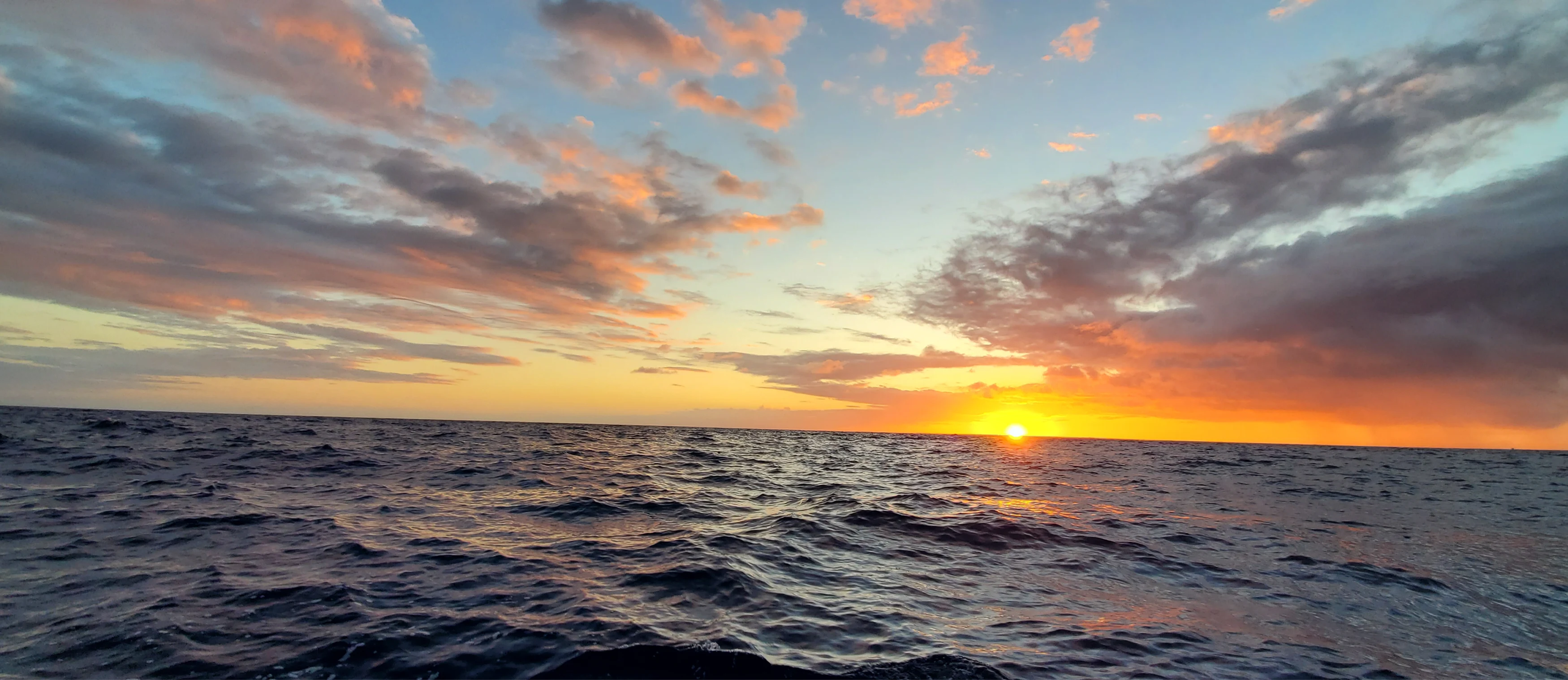 Ocean waves under a colorful sunset sky with scattered clouds at the horizon.