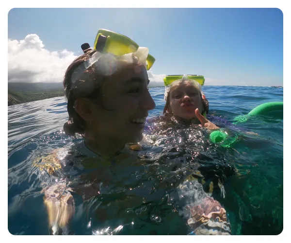 Two people snorkeling in clear ocean water with green snorkel masks on a sunny day.