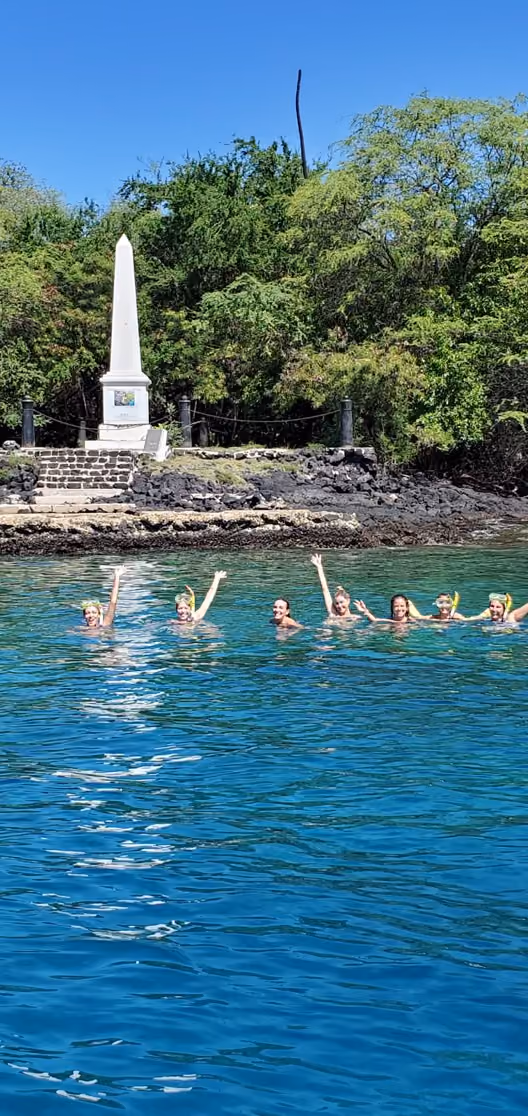 Snorkelers waving in front of the white Captain Cook Monument in Kealakekua Bay
