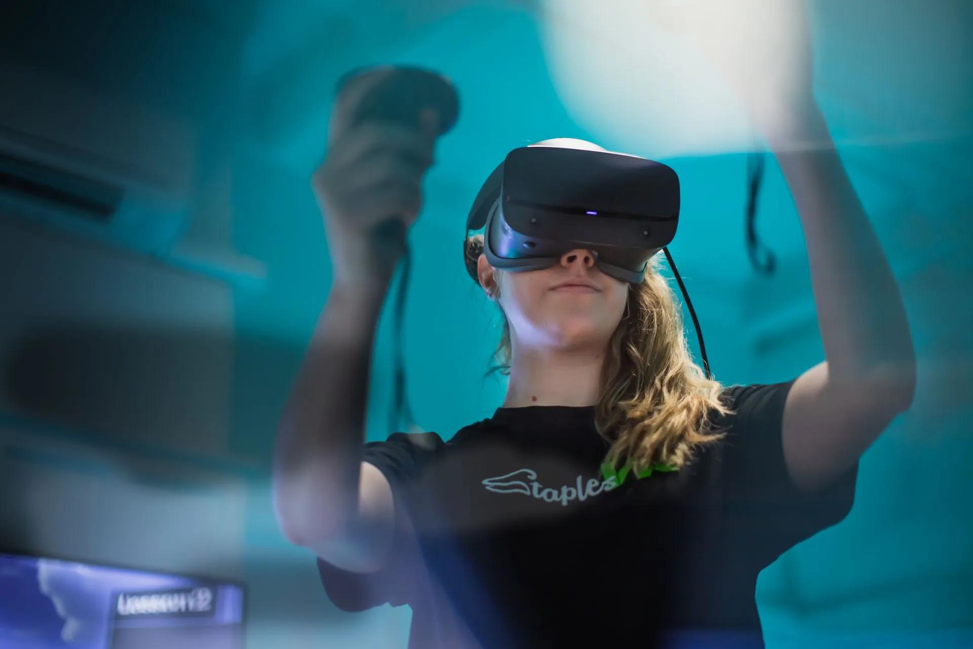 Woman wearing a virtual reality headset and holding VR controllers in a blue-lit room.