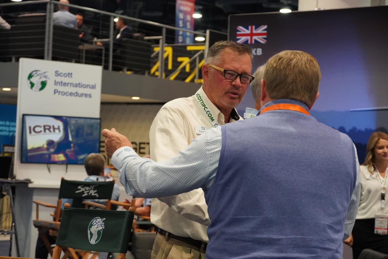 Scott IPC CEO Shawn Scott discussing international procedures with a client at the booth, the ICRH cockpit reference on screen