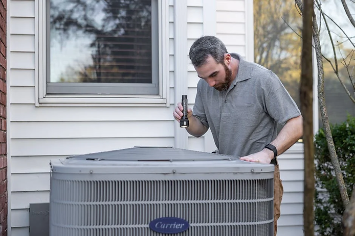 Man inspecting a heat pump unit with a flashlight, emphasizing the importance of maintenance and repair services for HVAC systems in Tacoma.